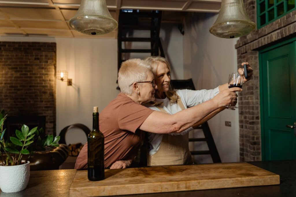Two senior women taking a selfie while enjoying wine in a cozy indoor setting.