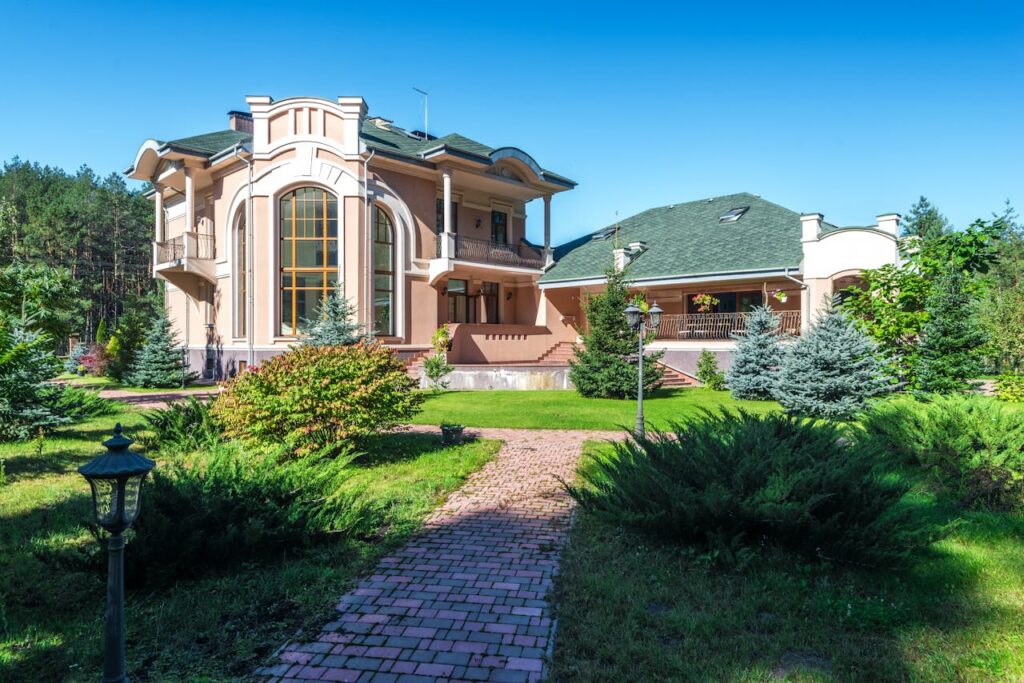 Beautiful mansion in sunny weather, surrounded by lush greenery and a clear blue sky.