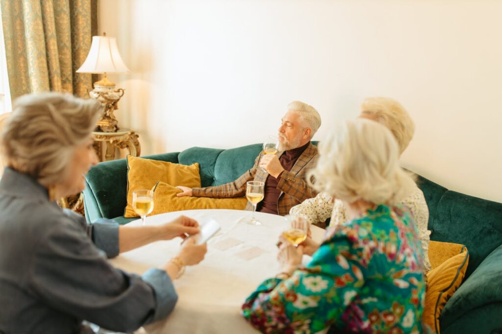 A group of senior adults enjoying wine and conversation in a cozy living room setting.